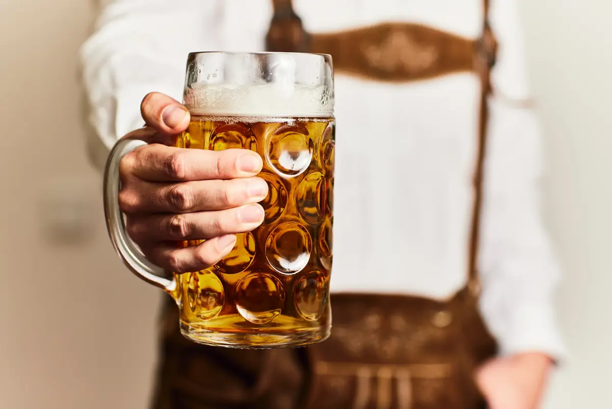 A person in traditional attire holds a large glass of beer with a foamy top.