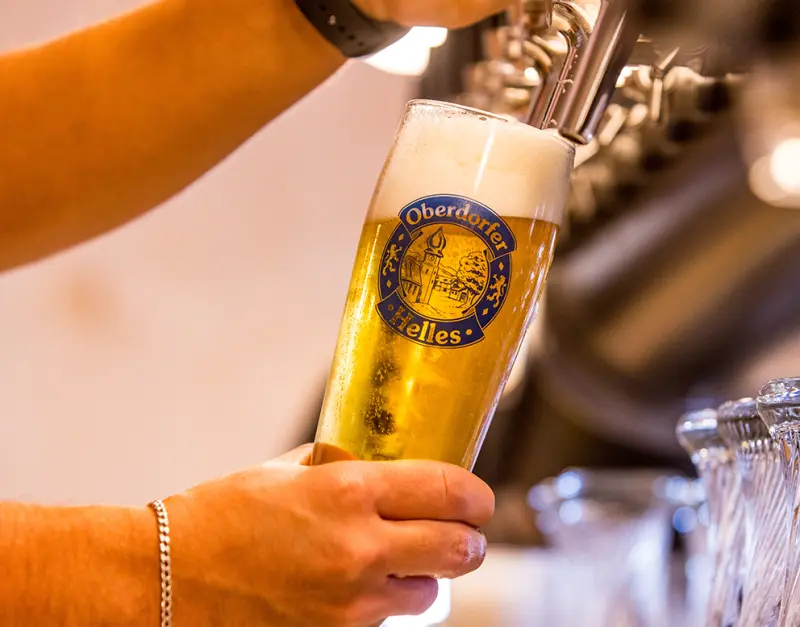 A person is pouring a golden beer into a branded glass from a tap.