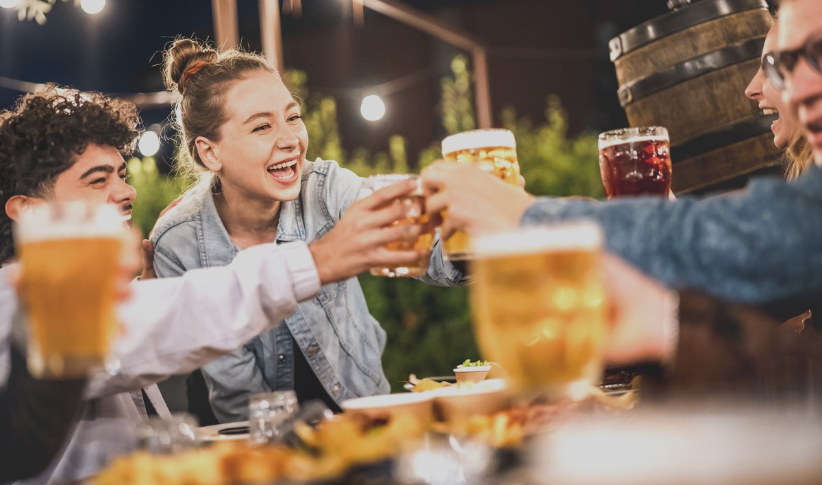 Four friends enjoy drinks and laughs together at an outdoor table at night.