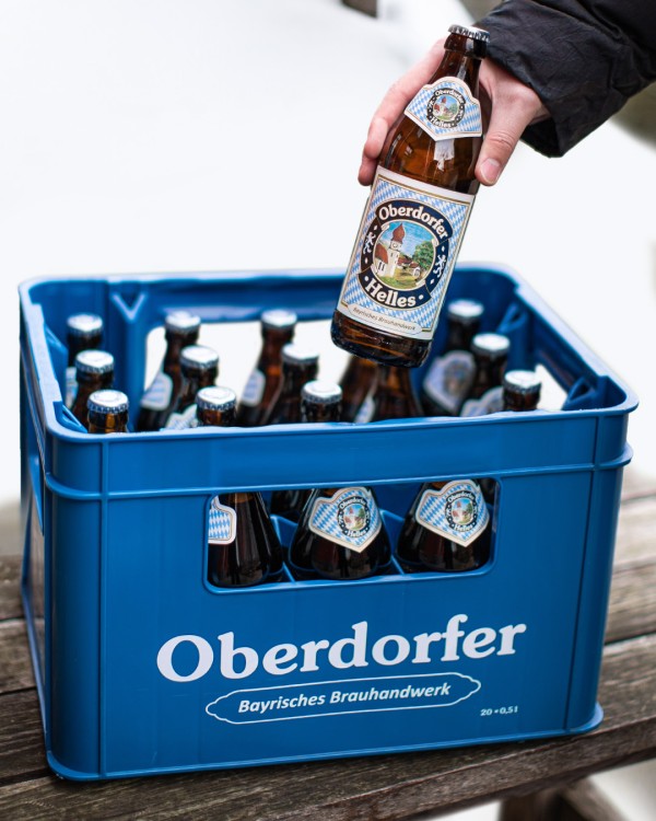 A hand is holding a bottle of beer above a blue crate filled with similar bottles.